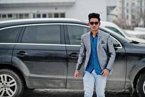 Casual young indian man in sunglasses posed against suv car. photo