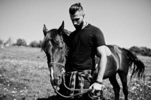 Hombre árabe de barba alta vestido de negro con caballo árabe. foto