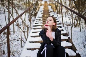 Fashionable long legs brunette model in long black cloak posed outdoor at winter day. photo