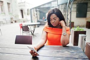 mujer afroamericana modelo xxl en vestido naranja mirando en el teléfono móvil. foto