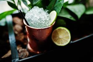 Alcoholic cocktail with ice and lime in bronze can glass on bar table. photo