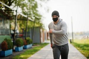 retrato deportivo hombre árabe con mascarilla médica negra correr al aire libre durante la cuarentena del coronavirus. foto