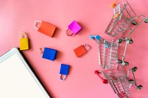 el concepto mínimo de compras en línea, la bolsa de compras de papel de colores y el carrito bajan del fondo rosa flotante para el espacio de copia. el cliente puede comprar todo desde su casa y el mensajero lo entregará. foto