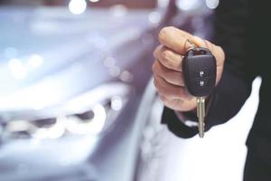 man wear leather jacket hand holding a button on the car keys remote control against blur car background. photo