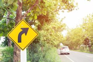 traffic sign placed beside along the road on route twisty winding slope. background driver car reduce speed and use a lower gear on country road. photo