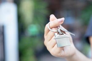 people hand holding house key on home shaped key chain. concept for buying real estate agent housing and apartment condominium. Leave space for writing text. photo