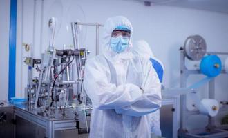 Technician worker wearing protective suite , glove are inspect machine with check  face mask manufacturing process to safe and against from virus photo