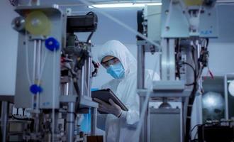 Technician worker wearing protective suite , glove are inspect machine with check  face mask manufacturing process to safe and against from virus photo