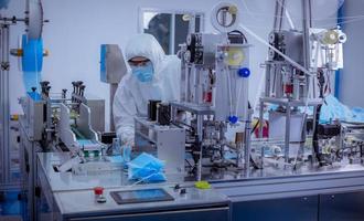 Technician worker wearing protective suite , glove are inspect machine with check  face mask manufacturing process to safe and against from virus photo