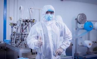 Technician worker wearing protective suite , glove are inspect machine with check  face mask manufacturing process to safe and against from virus photo