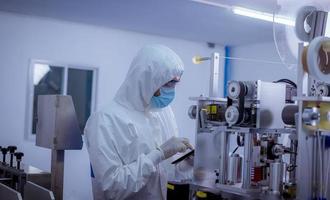 Technician worker wearing protective suite , glove are inspect machine with check  face mask manufacturing process to safe and against from virus photo