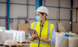 Factory engineer under inspection and checking quality production process on face mask manufacture  station by  wearing casual uniform and safety helmet in factory plantation. photo