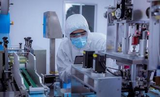 Technician worker wearing protective suite , glove are inspect machine with check  face mask manufacturing process to safe and against from virus photo