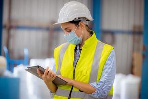 Factory engineer under inspection and checking quality production process on face mask manufacture  station by  wearing casual uniform and safety helmet in factory plantation. photo