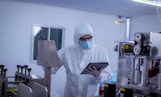 Technician worker wearing protective suite , glove are inspect machine with check  face mask manufacturing process to safe and against from virus photo