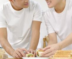 Two roll sandwich put on the plate with male couple hands, happy smiling face in the kitchen together. LGBT domestic life concept. Vertical cropped image. Selective focus. photo