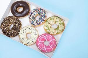 assorted donuts with chocolate frosting, topping sprinkles donuts Colorful variety and Variety of flavors mix of multi colored sweet donuts with frosted sprinkled on blue background. top view photo