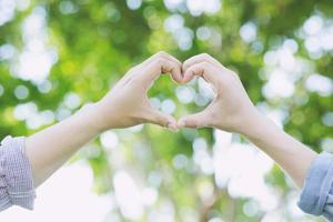 Supporting hands make heart sign and wave in front of a rainbow flag flying on the sidelines of a summer gay pride parade photo