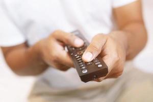 close up Television remote control in casual man hands pointing to tv set and turning it on or off. select channel watching tv on his sofa at home in the living room relax. photo