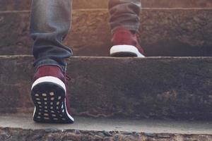 escalera. cerrar las piernas jeans y zapatos zapatillas rojas de un joven hipster una persona caminando subiendo las escaleras en la ciudad moderna, subir escaleras, éxito, crecer. sol de la mañana. foto