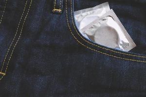 el hombre del condón listo para usar en el bolsillo de los jeans, da el concepto de sexo seguro del condón en la cama para prevenir infecciones y los anticonceptivos controlan la tasa de natalidad o la profilaxis segura. día mundial del sida, deja espacio para el texto. foto