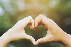 Young couple lover show holding hands make heart shape over in public parks. photo