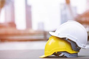 sombrero de casco de seguridad duro amarillo y blanco en el proyecto en el edificio del sitio de construcción en el piso de concreto en la ciudad con luz solar. casco para obrero como ingeniero o trabajador. concepto de seguridad primero. foto