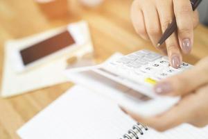Close up young woman hand is writing in a notebook and using calculator counting making notes Accounting at doing finance at home office.  Savings finances concept. note pad photo