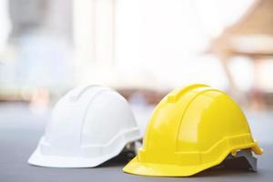 sombrero de casco de seguridad duro amarillo y blanco en el proyecto en el edificio del sitio de construcción en el piso de concreto en la ciudad con luz solar. casco para obrero como ingeniero o trabajador. concepto de seguridad primero. foto