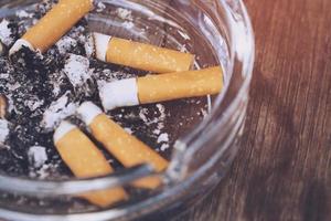 Ashtray full of cigarettes butts close-up on wood background