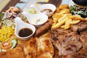 Fast food concept with greasy grill fried restaurant take out as Succulent thick juicy portions of grilled fillet steak served, burger and hot dogs,french fries,vegetable salad sauce on  Wooden plate. photo
