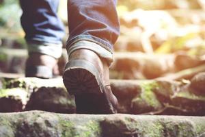 viajero turista excursionista zapatos de primer plano botas y bastones de senderismo bastones. hombre excursionistas turísticos caminando en el sendero de los escalones del bosque en un tronco de madera con sol. concepto de viaje foto