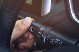 close up hand adjusting rain windscreen wiper knob control stick switch speed of screen front car. Adjustable wiper blade remove dirt from the windshield. Modern car interior detail. photo