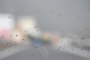 gotas de lluvia lloviznan en el parabrisas de cristal por la noche. calle bajo la fuerte lluvia. Bokeh luz trasera y semáforos en la ciudad. conduzca el automóvil con cuidado, camino resbaladizo. enfoque suave. foto