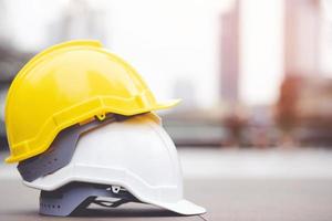 sombrero de casco de seguridad duro amarillo y blanco en el proyecto en el edificio del sitio de construcción en el piso de concreto en la ciudad con luz solar. casco para obrero como ingeniero o trabajador. concepto de seguridad primero. foto