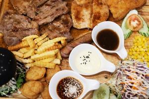 Fast food concept with greasy grill fried restaurant take out as Succulent thick juicy portions of grilled fillet steak served, burger and hot dogs,french fries,vegetable salad sauce on  Wooden plate. photo