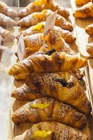 varios sabores de croissant o como en italia se llaman brioche en exhibición en una panadería en milán, italia con un precio y un cartel - albicocca significa mermelada en italiano foto