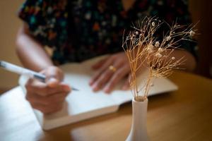 Vase decorated by dried flowers, woman taking note as soft focused background. photo