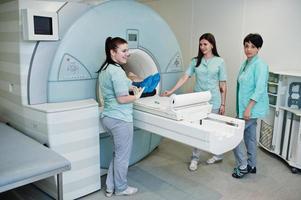 Three female doctors near magnetic resonance imaging machine with patient inside. photo