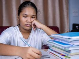 girl doing homework on a wooden table and there was a pile of books next to it The background is a red sofa and cream curtains. photo