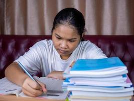 girl doing homework on a wooden table and there was a pile of books next to it The background is a red sofa and cream curtains. photo