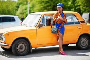 bella dama afroamericana parada cerca de un auto retro clásico naranja. foto