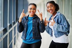 dos amigas africanas con chaqueta de jeans muestran dedos de roca juntos en el interior. foto