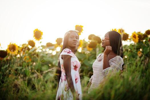 dos jóvenes amigas negras usan pose de vestido de verano en un campo de girasoles. foto