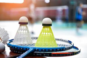 volante de bádminton blanco crema y raqueta con sombreado de luz de neón en el suelo verde en la cancha de bádminton cubierta, fondo de bádminton borroso, espacio para copiar. foto