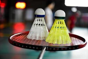 White and yellow plastic badminton shuttlecock and racket with neon light shading on green floor in indoor badminton court, blurred badminton background, copy space. photo