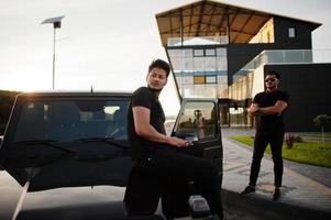 Two asian brothers man wear on all black posed near suv car. photo