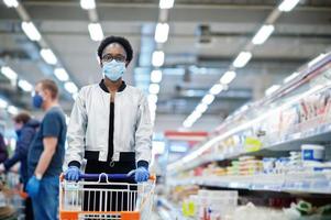 mujer africana con máscara médica desechable y guantes comprando en un supermercado durante el brote de pandemia de coronavirus. tiempo de epidemia.
