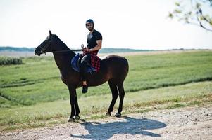 El hombre árabe de barba alta usa casco negro, monta un caballo árabe. foto