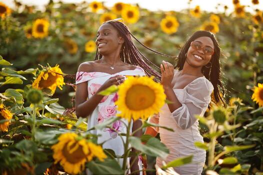 dos jóvenes amigas negras usan pose de vestido de verano en un campo de girasoles. foto